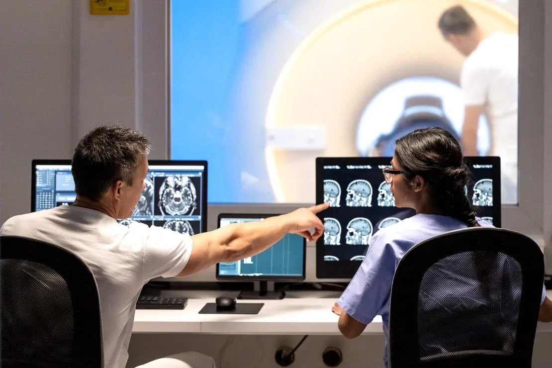 Back view of two doctors analyzing MRI scan results. Man pointing at images on monitor screen. Magnetic resonance imaging technology in specialized medical clinic.