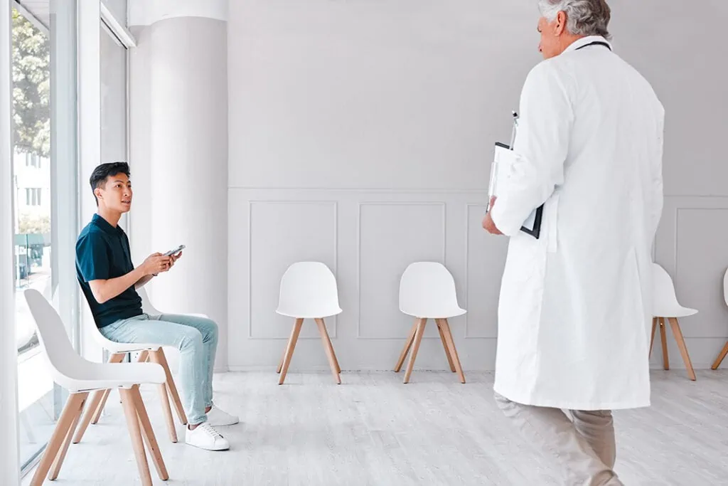 Aufnahme eines jungen Mannes, der ein Handy benutzt, während er im Wartezimmer einer Klinik sitzt