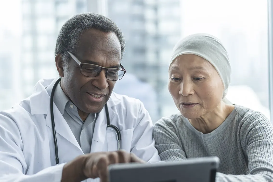 Ein Arzt blickt gemeinsam mit einer Patientin mit Kopftuch auf ein Tablet und zeigt ihr z.B. Untersuchungsergebnisse aus ihrer elektronischen Patientenakte